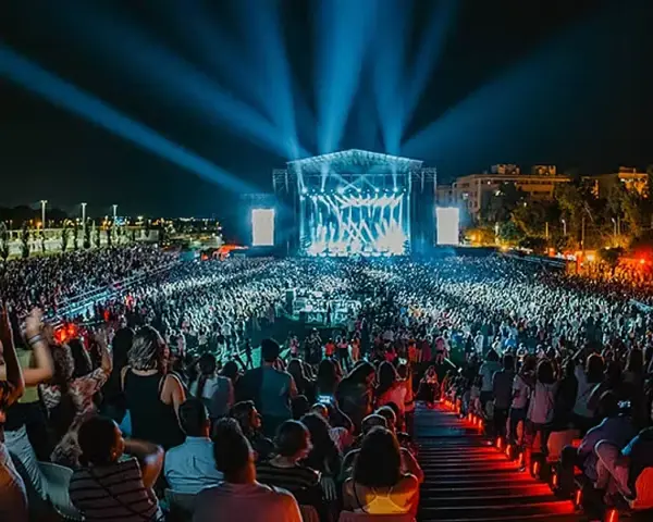 Multitud en un concierto nocturno, luces azules iluminan el escenario y al público. Un evento vibrante, como un **cabaret mairena** moderno.