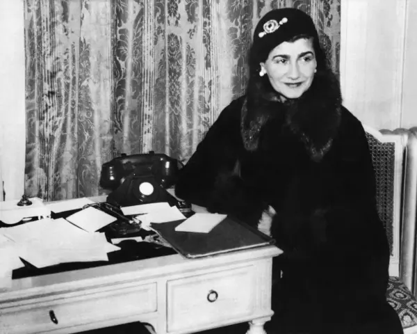 Coco Chanel, icona di stile, al suo scrittoio. La sua storia è fatta di eleganza e innovazione.