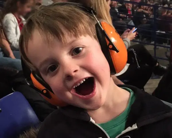 Un jeune garçon de 3 ans, avec un bouchon oreille enfant 3 ans, sourit à pleines dents, prêt pour le spectacle.