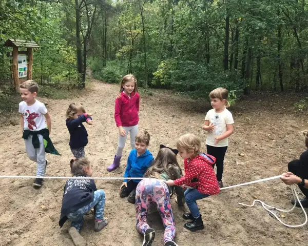 Grupa dzieci w wieku 6-12 lat bierze udział w przeciąganiu liny w lesie. Wszyscy świetnie się bawią!