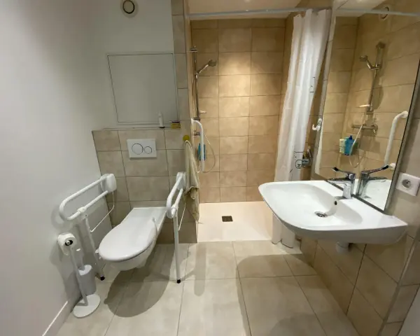 Salle de bain pmr avec douche à l'italienne, WC avec barres d'appui et lavabo. Confort et sécurité pour tous.
