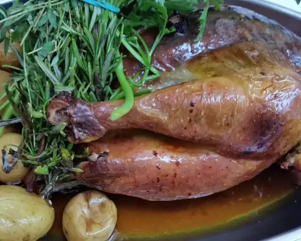 Pollo de Bresse asado, dorado y jugoso, acompañado de patatas pequeñas y hierbas frescas.