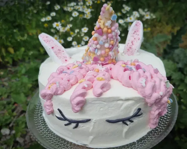 En förtrollande unicorn tårta med rosa glasstrut-liknande horn, dekorerad med strössel och blommor i bakgrunden.