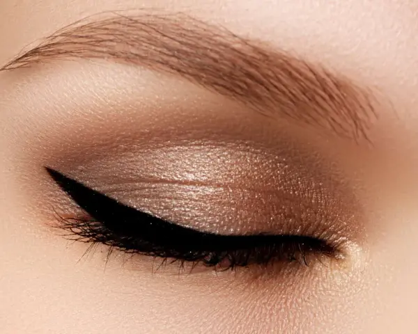 Occhio con trucco cat eyes, eyeliner nero definito e ombretto bronzo scintillante. Sopracciglio curato.