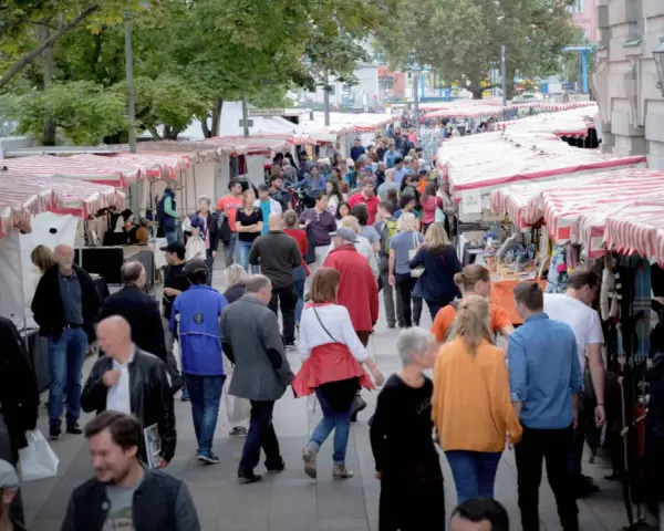 Menschen schlendern über einen belebten kunstmarkt berlin mit vielen Ständen und bunten Markisen.