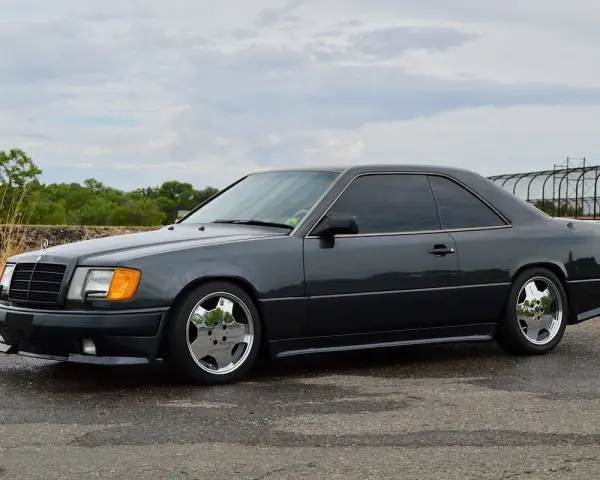 Ciemnoszary Mercedes "Hammer" coupe z przyciemnianymi szybami i chromowanymi felgami stoi na mokrej drodze.