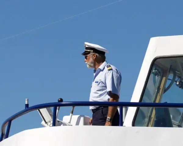 Kapitan na mostku statku, w białym mundurze i czapce, spogląda w dal. Zastanawiasz się, ile zarabia marynarz?