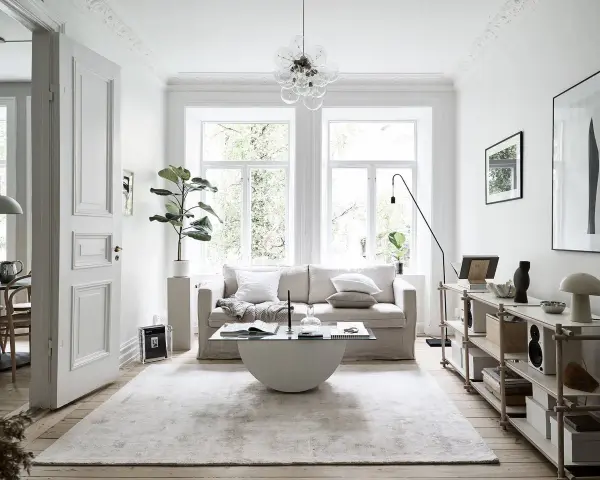 Salón con sofá beige, mesa de centro de cristal y alfombra clara. Decoración minimalista y plantas, creando un ambiente de feng shui.