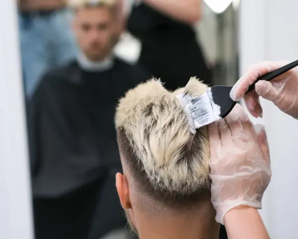 Fryzjer nakłada farbę na blond włosy mężczyzny.