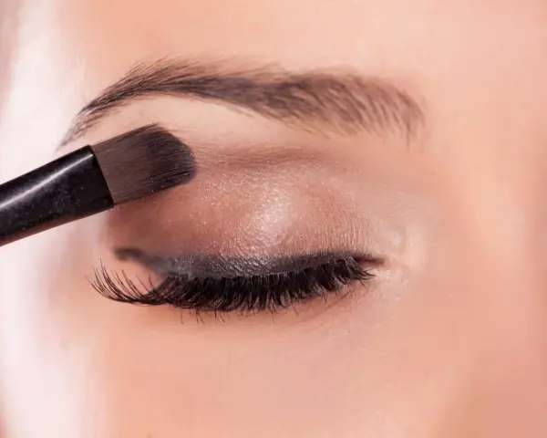 Application d'un fard à paupières marron pour un regard smoky intense.