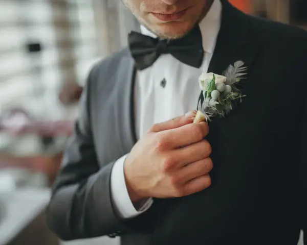 Mężczyzna poprawia butonierkę w eleganckim, czarnym garniturze.
