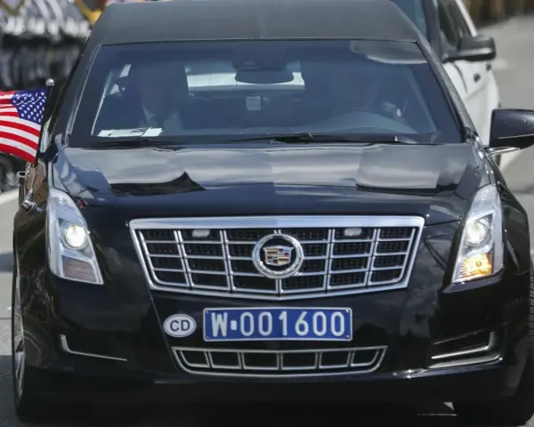 Czarny Cadillac z amerykańską flagą i tablicą rejestracyjną CD W-001600, wskazującą na rejestracje dyplomatyczne.