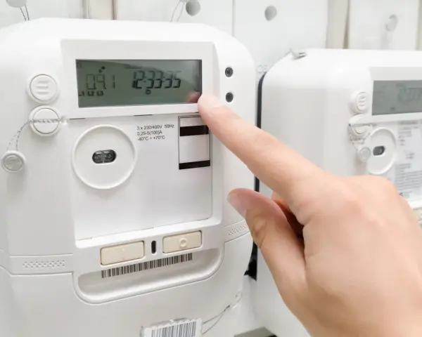 Palec naciska przycisk licznika energii elektrycznej, sprawdzając opłatę mocową.