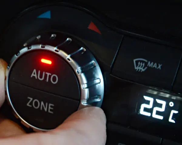 Hand dreht am Regler der **Klimaanlage Auto** auf 22 Grad Celsius. Rote LED leuchtet.
