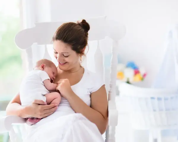Uśmiechnięta mama kołysze śpiące dziecko. Gratulacje z okazji narodzin dziecka!