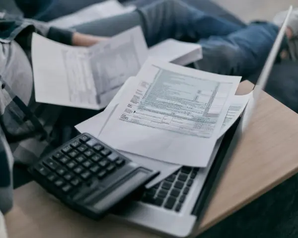 Osoba przegląda dokumenty podatkowe, kalkulator i laptop. Analiza składnik zmienny stawki sieciowej.