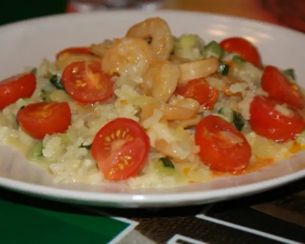 Risotto z krewetkami i pomidorkami koktajlowymi na białym talerzu.