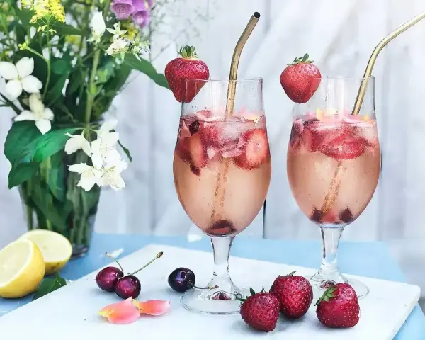 Två glas med ett uppfriskande drink med gin, fyllda med is, jordgubbar och körsbär. En perfekt sommardrink!