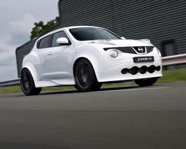 Biały Nissan Juke-R pędzi po torze, jego sportowy wygląd podkreślają szerokie nadkola i agresywny przedni zderzak.