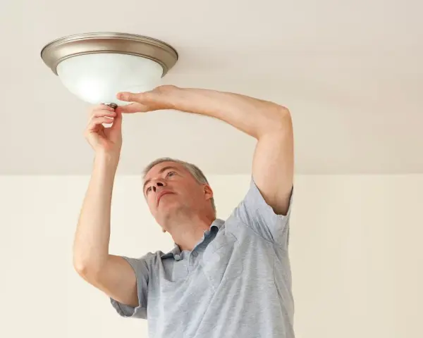 Mężczyzna wymienia żarówkę w lampie sufitowej, wykonując retrofit LED.