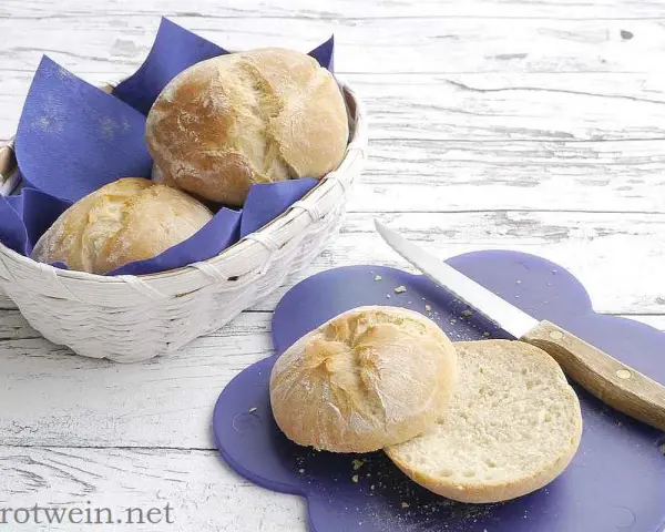 Frisch gebackenes, weiches Brot liegt in einem Korb und auf einem lila Brett. Ein Messer liegt daneben.