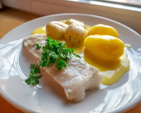 En portion rimmad torsk med kokt potatis och en krämig sås, garnerad med färsk persilja.