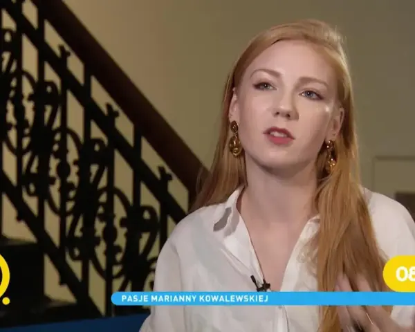 Marianna Kowalewska w białej koszuli, z rudymi włosami i złotymi kolczykami, opowiada o swoich pasjach na tle schodów.
