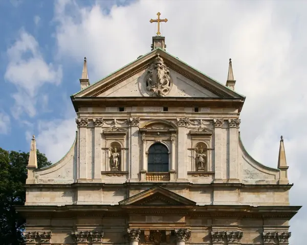 Bogata fasada kościoła w stylu barokowym, z rzeźbami i zdobieniami, pod błękitnym niebem.