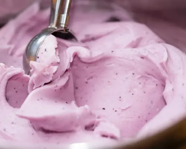 Ein Löffel nimmt eine Kugel cremiges, lila Beeren-Eis aus Milch.
