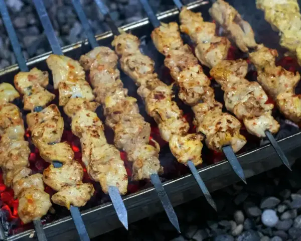 Aromatyczny kebab z kurczaka na rozżarzonych węglach. Soczyste kawałki mięsa pieką się na szpikulcach, tworząc apetyczny widok.