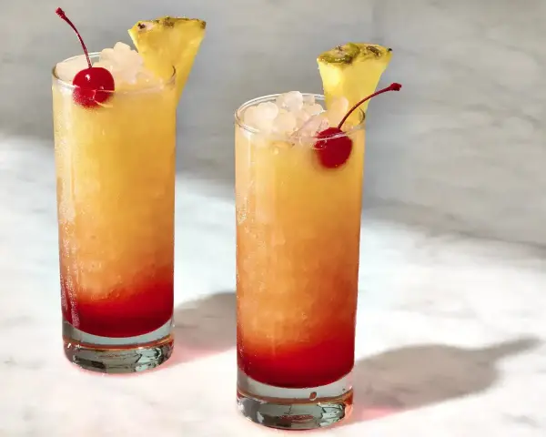 Dwa drinki z Malibu z sokiem ananasowym, lodem, wiśnią i plasterkiem ananasa. Idealne na upalne dni.