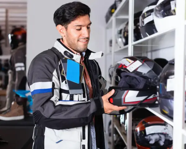 Uomo in negozio di moto esamina un casco, cercando la taglia XS. Corrisponde a una misura piccola, ideale per teste più minute.