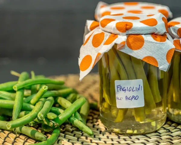 Fagiolini sott'olio in agrodolce, conservati in barattoli con tappi decorati. Freschi e pronti per essere gustati.