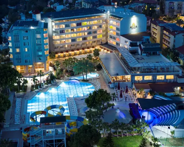 Nocny widok na Meridia Beach Hotel z oświetlonymi basenami, zjeżdżalniami i restauracją.