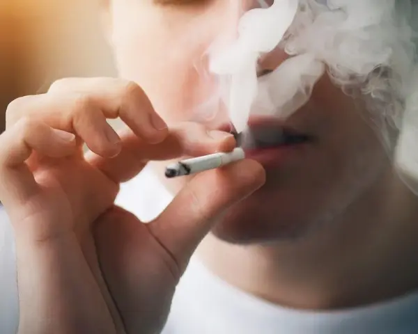 Persona fumando un cigarrillo, exhalando humo denso. Podría ser un indicio de sobredosis de nicotina.