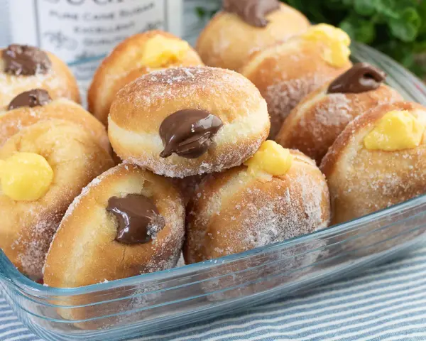 Bomboloni ricetta originale ripieni di crema e cioccolato, cosparsi di zucchero. Un dolce invitante pronto da gustare.