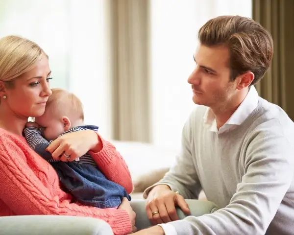 Zmartwiona mama tuli dziecko, a ojciec patrzy z troską. Czy to baby blues? Co to za uczucie?