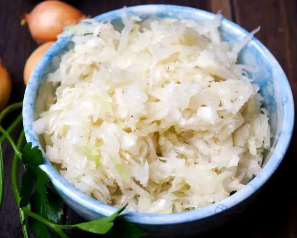 Schüssel mit frischem Krautsalat, daneben Zwiebeln und Petersilie. Perfekt für ein leckeres Krautsalat Rezept.