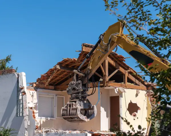 Kruszarka koparki niszczy budynek, realizując pozwolenie na rozbiórkę budynku w granicy działki.