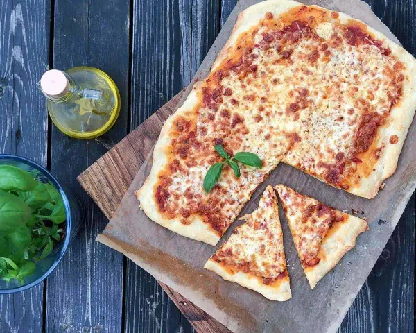 Pyszna pizza margherita z ciągnącym się serem i świeżą bazylią, obok butelka oliwy i miseczka ziół.