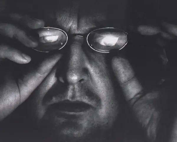Portret Krzysztofa Gierałtowskiego w okularach, z dłońmi przy twarzy.