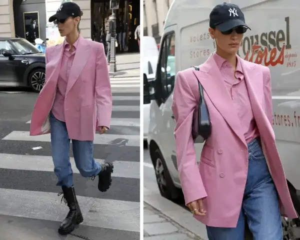 Kobieta w marynarce w odcieniu **magenta kolor** i jeansach idzie ulicą. Czapka z daszkiem i okulary dodają jej miejskiego stylu.