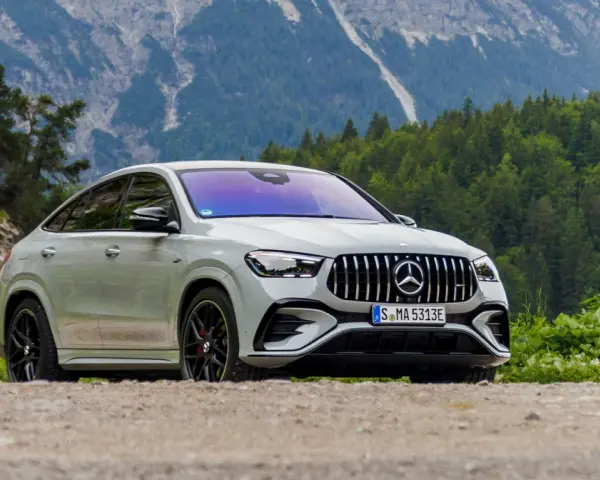 Biały Mercedes GLE 53 AMG coupe na tle górskiego krajobrazu z lasem.