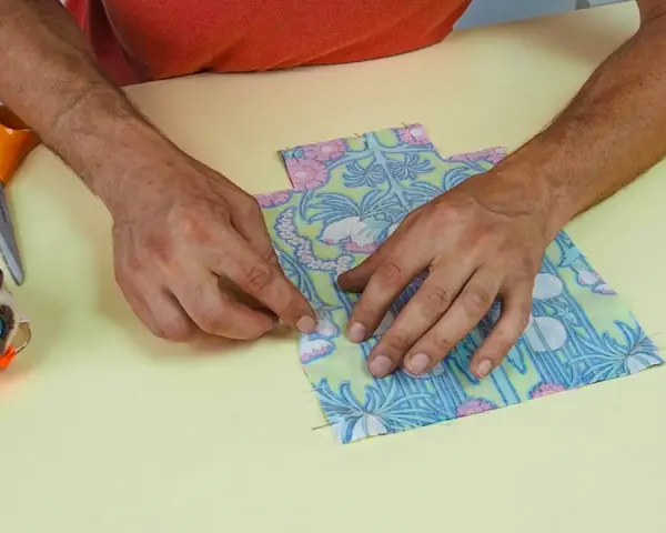 Mains assemblant deux pièces de tissu fleuri, parfait pour une idée couture débutant. Ciseaux et un chat porte-épingles à proximité.