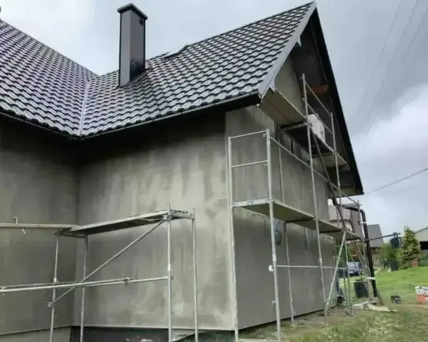 Dom w trakcie prac elewacyjnych. Widać rusztowania i szarą ścianę, która czeka na tynk silikonowy. Cena za m2 robocizny jest kluczowa dla budżetu.