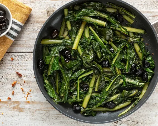 Verdura di catalogna saltata in padella con olive nere. Un piatto semplice e gustoso, pronto per essere servito.