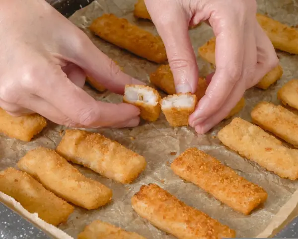 Ręce rozdzielają chrupiące paluszki rybne. Idealne na szybki obiad, warto sprawdzić paluszki rybne kcal.