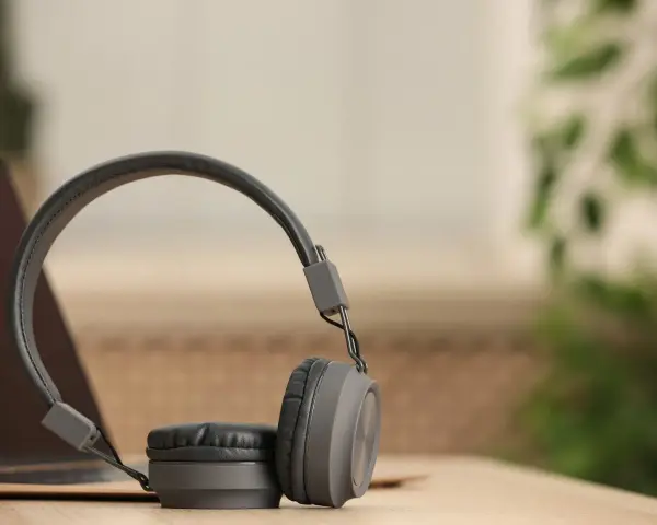 Szare słuchawki dynamiczne na drewnianym blacie, obok laptopa. Idealne do słuchania muzyki i podcastów.