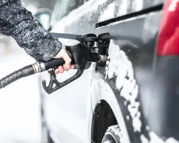 Ręka w zimowej kurtce trzyma pistolet do tankowania, nalewając diesel paliwo do samochodu podczas opadów śniegu.
