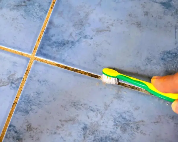 Main tenant utilise une brosse à dents pour nettoyer joint carrelage.